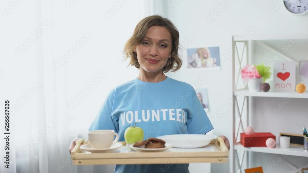 Young smiling volunteer holding tray with breakfast food in hands, kindness Young smiling volunteer holding tray with breakfast food in hands, kindness