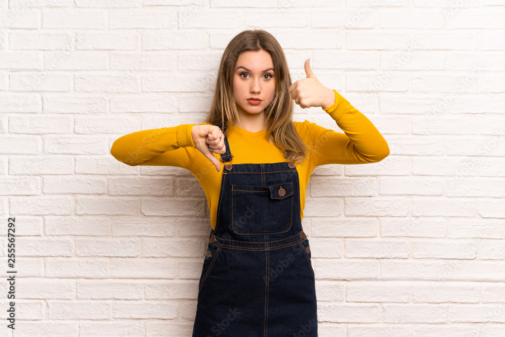 Teenager girl over white brick wall making good-bad sign. Undecided between yes or not Teenager girl over white brick wall making good-bad sign. Undecided between yes or not