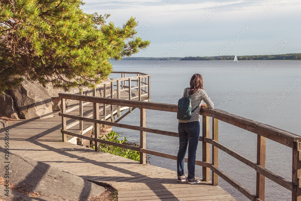 Wooden Pathway or Footpath near lake. Path along the water. Beautiful landscape with way between stones and lake. Swedish nature. Woman looks into the distance. Wooden Pathway or Footpath near lake. Path along the water. Beautiful landscape with way between stones and lake. Swedish nature. Woman looks into the distance.