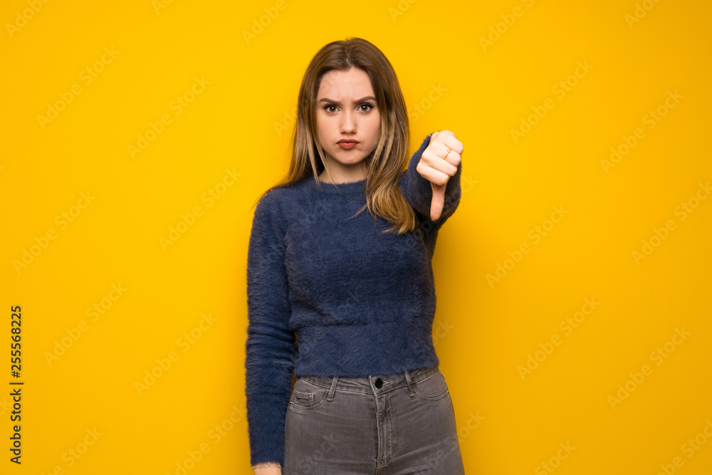 Teenager girl over yellow wall showing thumb dowg with negative expression Teenager girl over yellow wall showing thumb dowg with negative expression