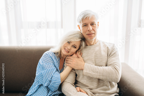 Mature husband and wife sitting on couch and hugs