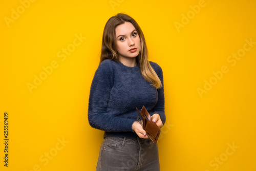 Teenager girl over yellow wall holding a wallet