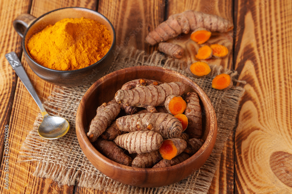 Turmeric roots and powder in bowls on old wooden table Turmeric roots and powder in bowls on old wooden table