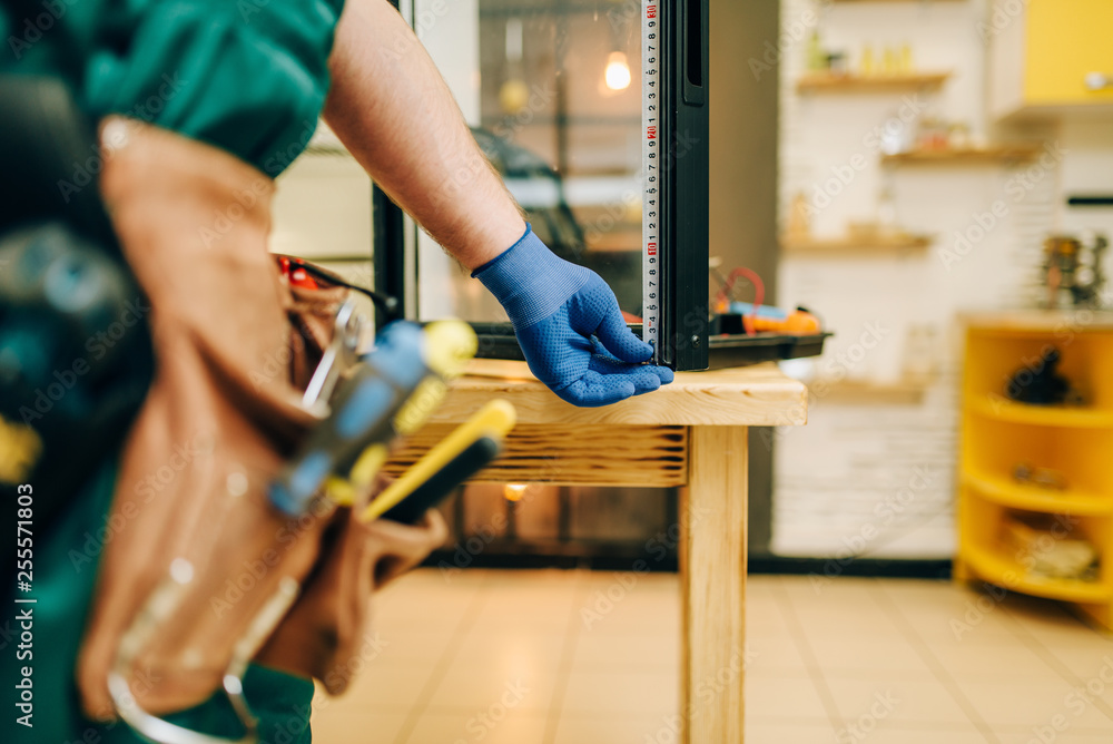 Repairman in uniform repairs refrigerator at home Repairman in uniform repairs refrigerator at home