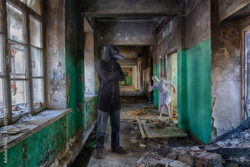 Tall man in plague doctor mask in hooded mantle and zombie monster nurse with knife. Horror movie scene in abandoned asylum or hospital