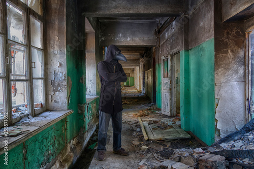 Tall man in leather plague doctor  mask and mantle with hood inside abandoned building. Monster or ghost for horror © evgenzz