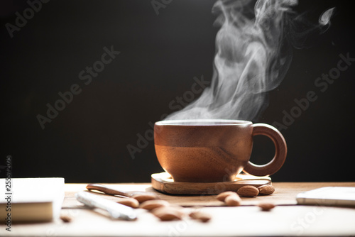 Hot tea with steam in wood cup and almonds on the wooden table black background.
