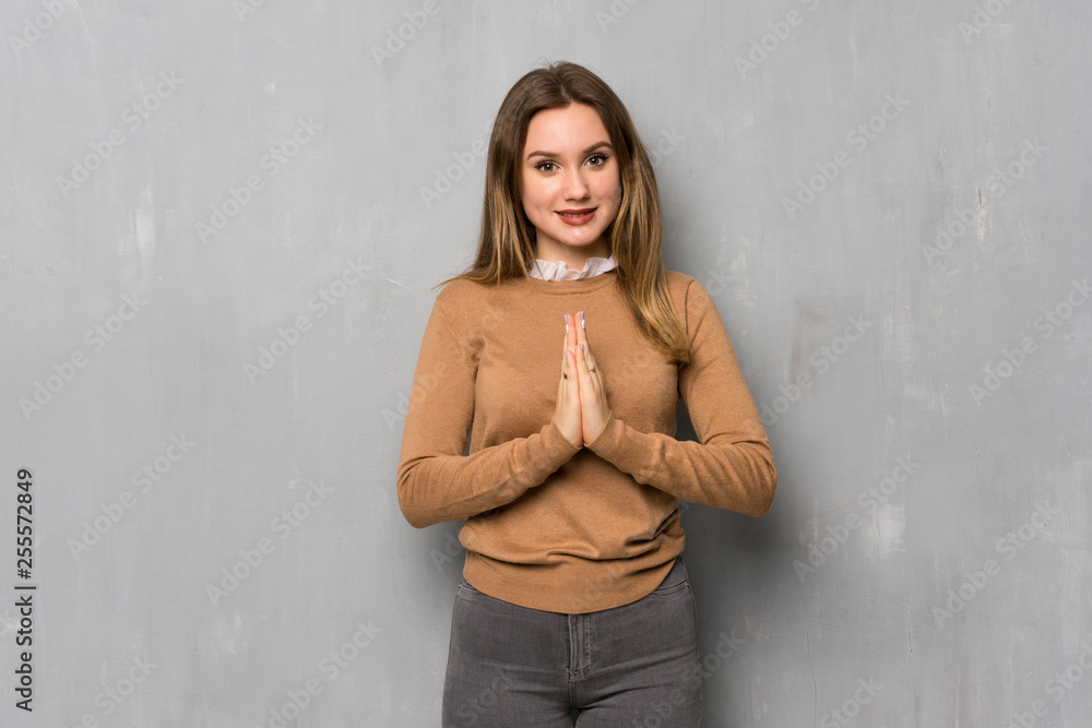 Teenager girl over textured wall keeps palm together. Person asks for something Teenager girl over textured wall keeps palm together. Person asks for something