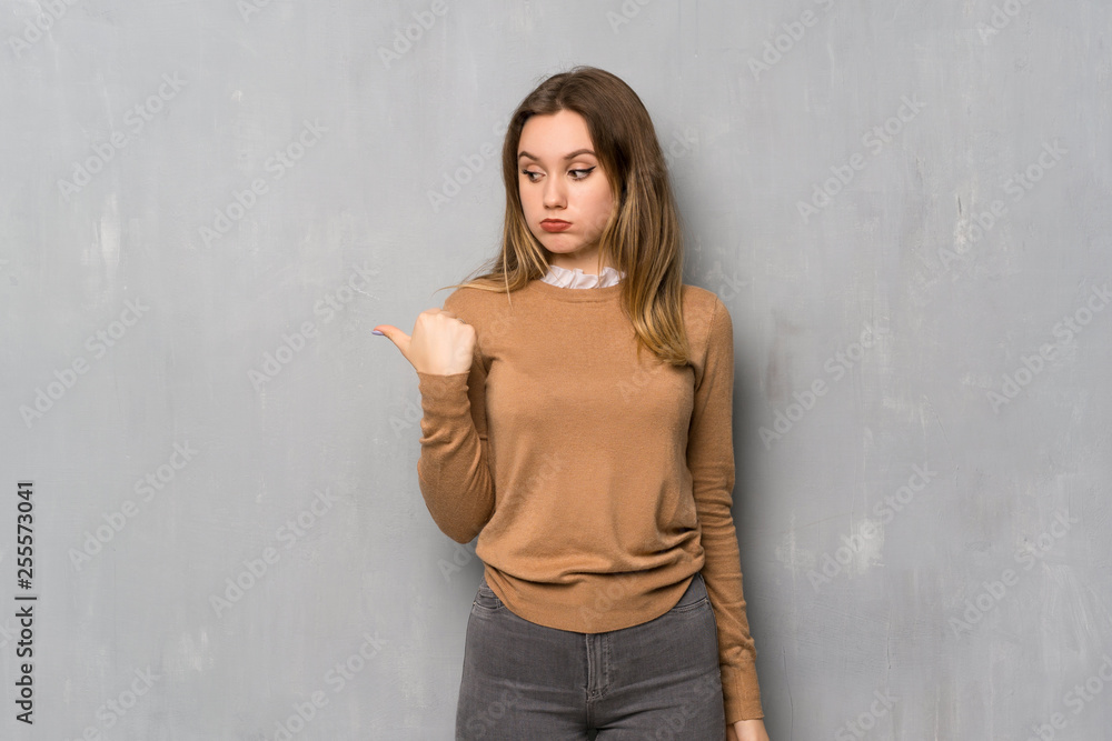 Teenager girl over textured wall unhappy and pointing to the side Teenager girl over textured wall unhappy and pointing to the side