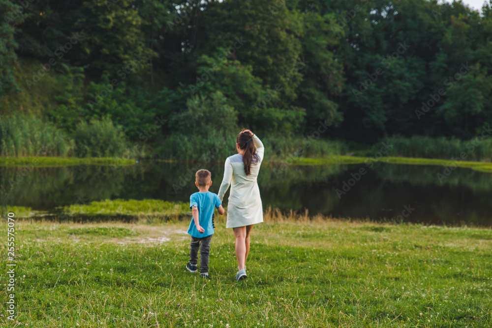 Fototapeta premium mother with kid holding hands walking to lake