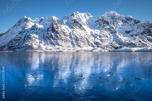 Blue ice covered fjord with mountain range in background on the Lofoten Islands in Norway in winter