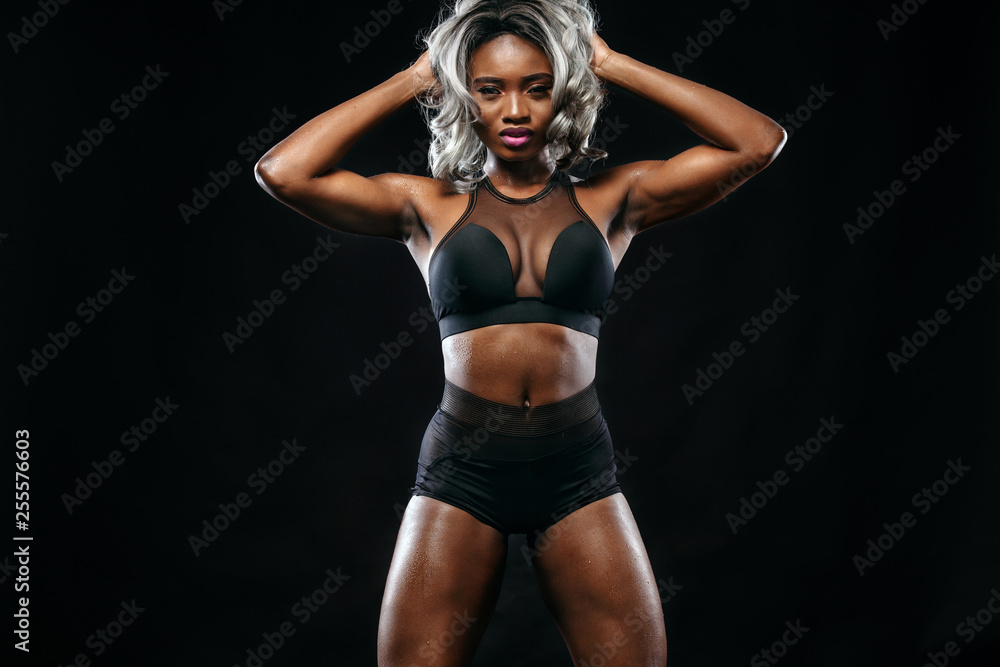 Sporty beautiful afro-american bodybuilder model, woman in sportwear makes fitness exercising at black background to stay fit