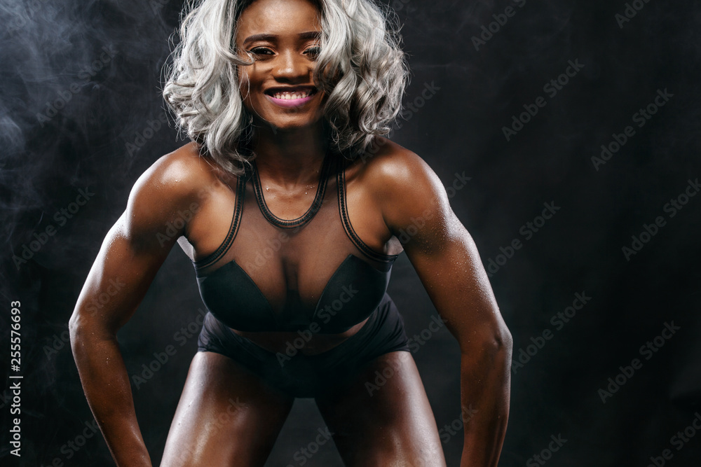 Sporty beautiful afro-american bodybuilder model, woman in sportwear makes fitness exercising at black background to stay fit Sporty beautiful afro-american bodybuilder model, woman in sportwear makes fitness exercising at black background to stay fit