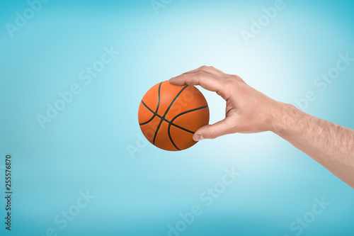 Side close-up of man's hand holding little basketball on light-blue background.