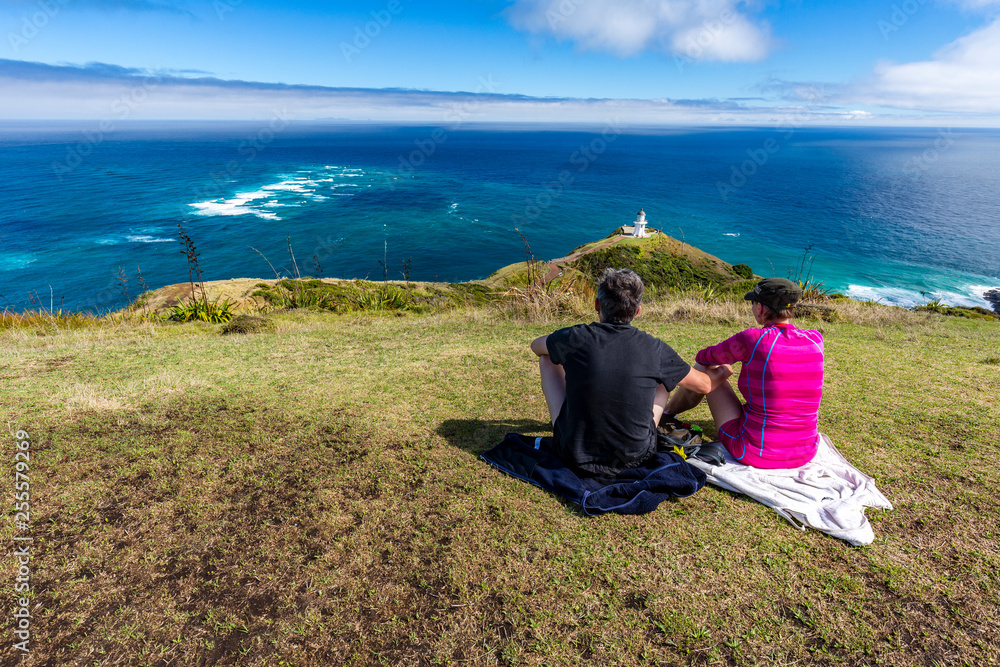 Couple enjoying the view Lighthouse at Cape Reinga, with Tasman Sea and Pacific, Northland, New Zealand