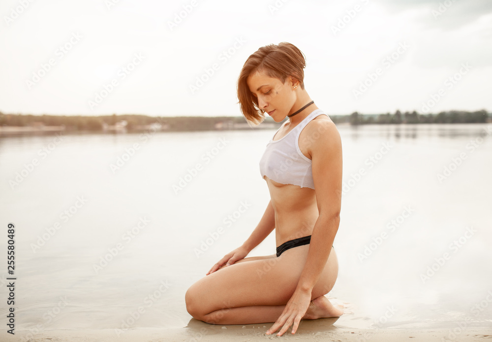 Summer. Beautiful girl with a short haircut on the beach. Sexy woman with  perfect sporty figure in black swimming trunks and short tank top. Stock  Photo | Adobe Stock
