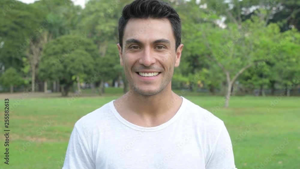 Face of happy young handsome Hispanic man smiling at the park Face of happy young handsome Hispanic man smiling at the park