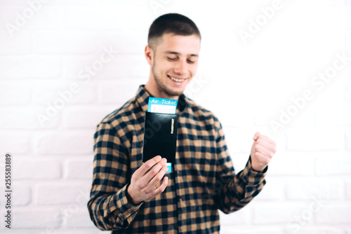 a handsome man in a plaid shirt against a brick wall with your passport and tickets inside