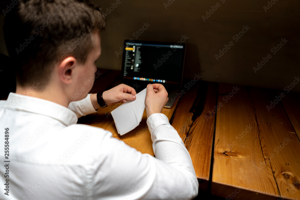 young businessman make origami on the wooden table in front of the laptop young businessman make origami on the wooden table in front of the laptop