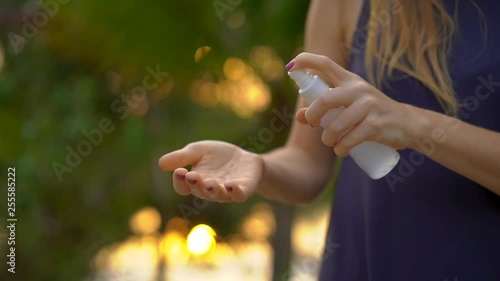 Superslowmotion shot of a beautiful young woman applying an antimosquito repellent spray on her skin. A tropical background. Mosquito defense concept photo