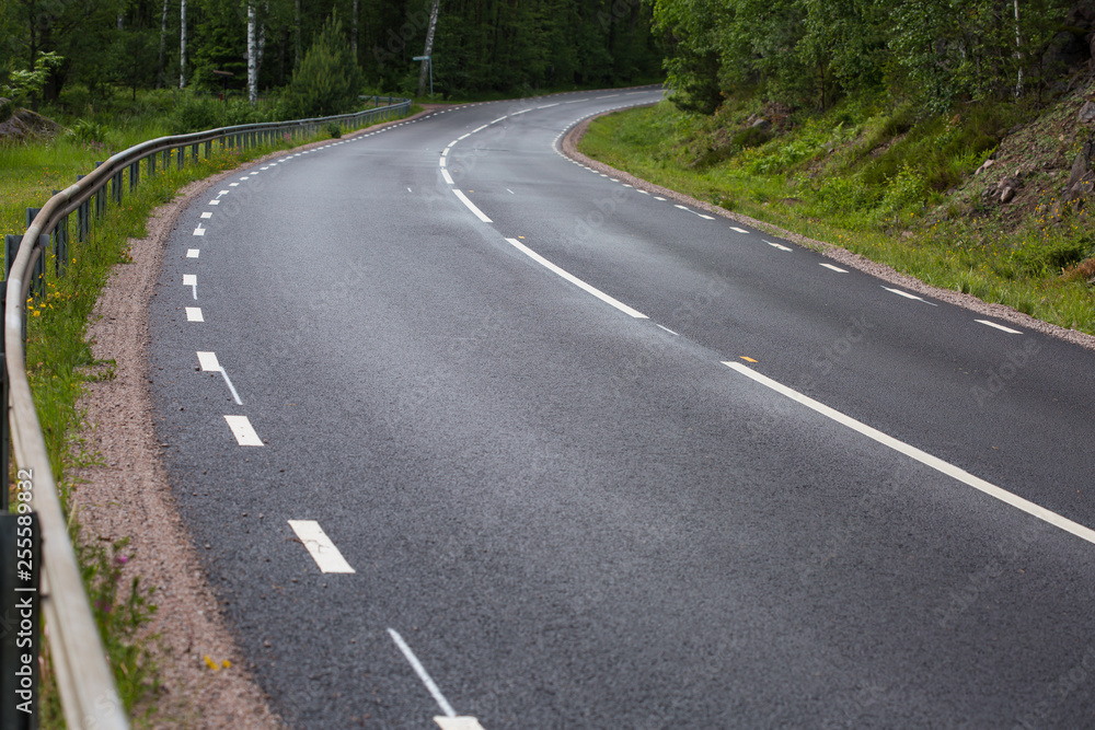 turn of the road with fresh traffic lane markings leading through thick north forest turn of the road with fresh traffic lane markings leading through thick north forest