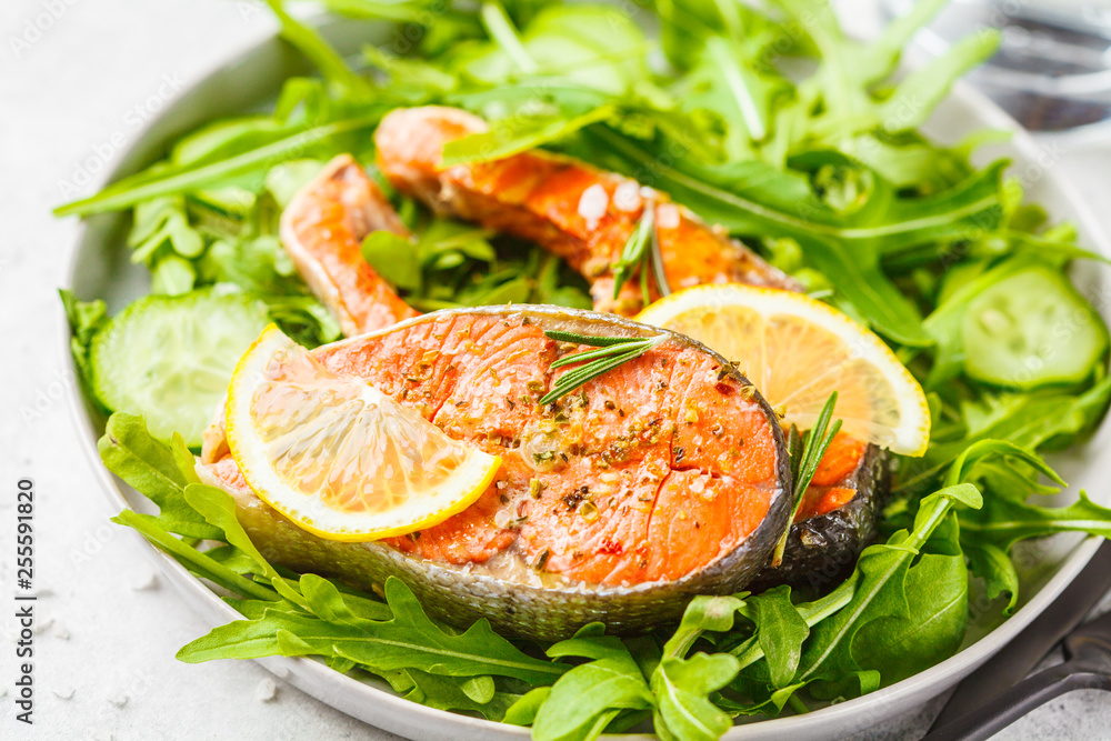 Fried red fish with arugula and cucumber salad in white plate.