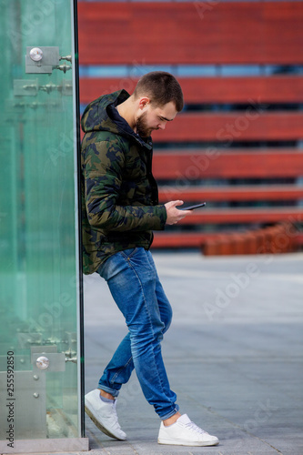 Young man texting on mobile phone on the city street.