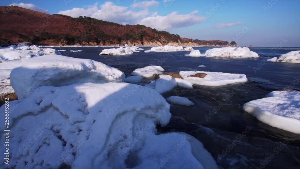 Panoramic view of coastline with forests growing on it. Big stones covered with snow on the foregroud and waves breaking at them. Clear sunny day. Marine biospheric reservation at Far East of Russia Panoramic view of coastline with forests growing on it. Big stones covered with snow on the foregroud and waves breaking at them. Clear sunny day. Marine biospheric reservation at Far East of Russia