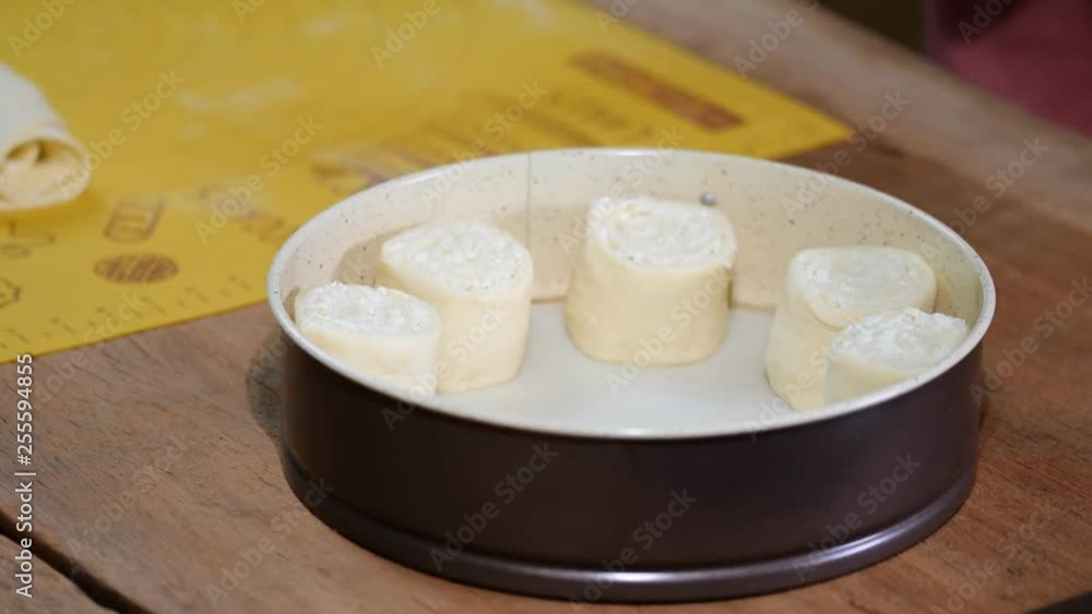 Female baker is putting buns to baking sheet, close up. Female baker is putting buns to baking sheet, close up.