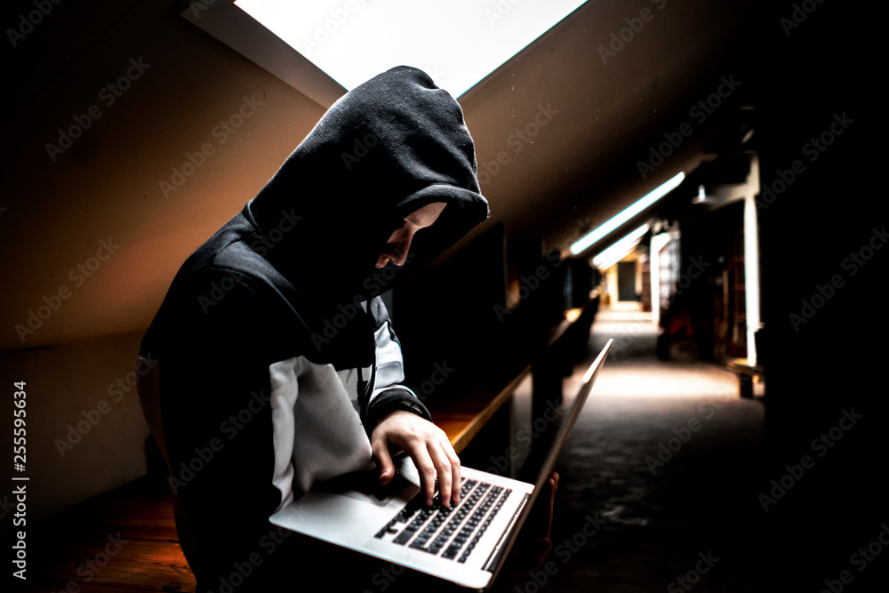 portrait of young geek in hood in dark room with laptop portrait of young geek in hood in dark room with laptop
