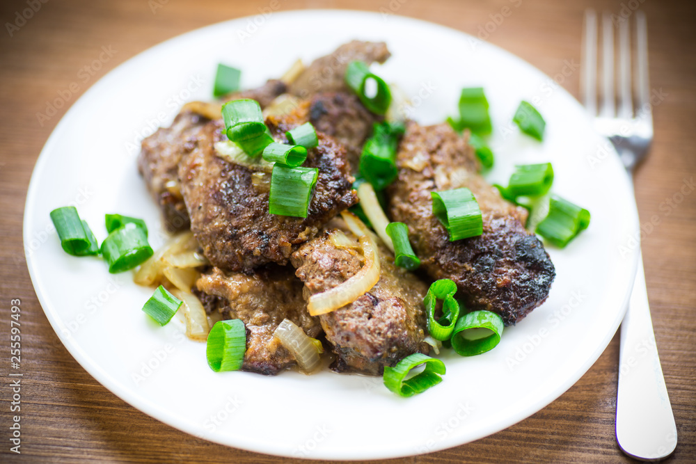 fried liver with onions in a plate on a wooden