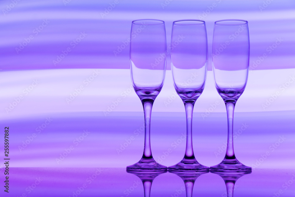 Three champagne glasses / flutes in a row with colorful multicolored light painting behind them Three champagne glasses / flutes in a row with colorful multicolored light painting behind them