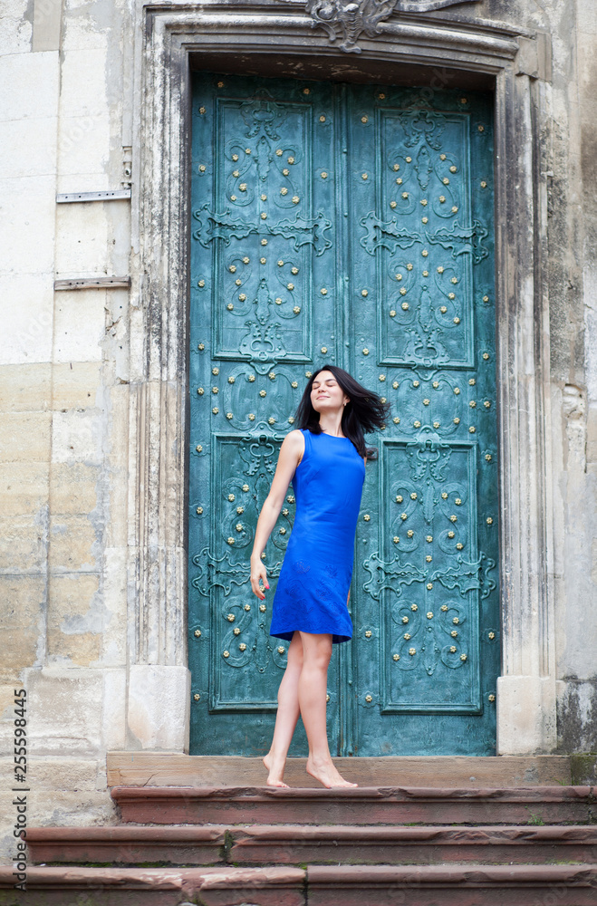 Young girl posing in a blue dress for the camera on a background of green metal door. Confident stylish woman looks to the side