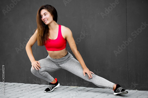 Sport fitness girl in fashion sportswear doing fitness exercise in the street, on gray wall background ,outdoor sports. Urban style.