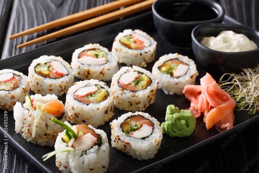 Uramaki rolls set served with sauces, soy sprouts, ginger and wasabi closeup on a plate. horizontal Uramaki rolls set served with sauces, soy sprouts, ginger and wasabi closeup on a plate. horizontal