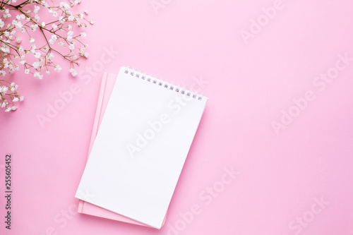 Empty notebook and white flowers on pink pastel table top view in flat lay style. Woman working desk. © KatrinaEra