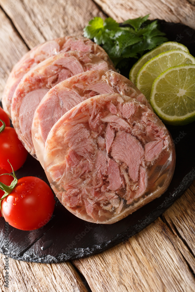 Delicious sliced Head cheese or brawn served with tomatoes, lime and cilantro closeup on a slate board. vertical