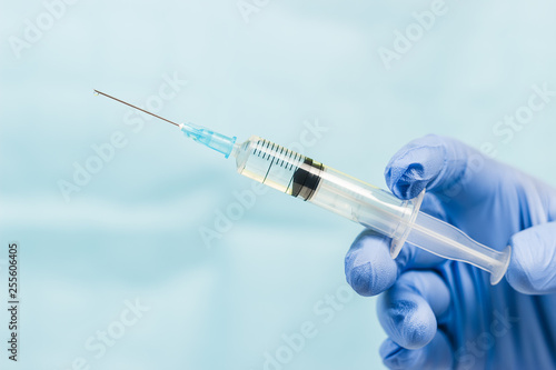 Blue gloved hand holding a syringe on blue background photo