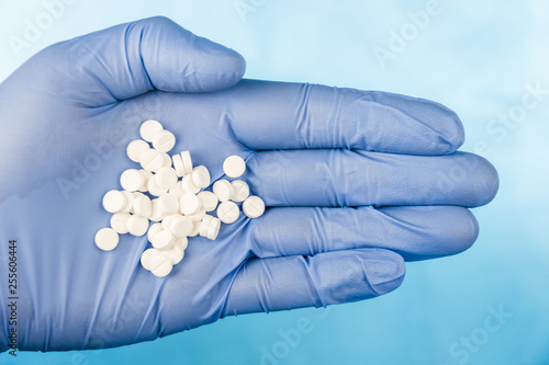 Blue-gloved hand pulls a handful of white pills
