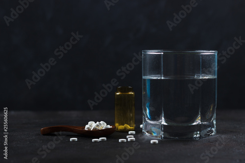 Tablets in a wooden spoon with a yellow empty can and a glass of water