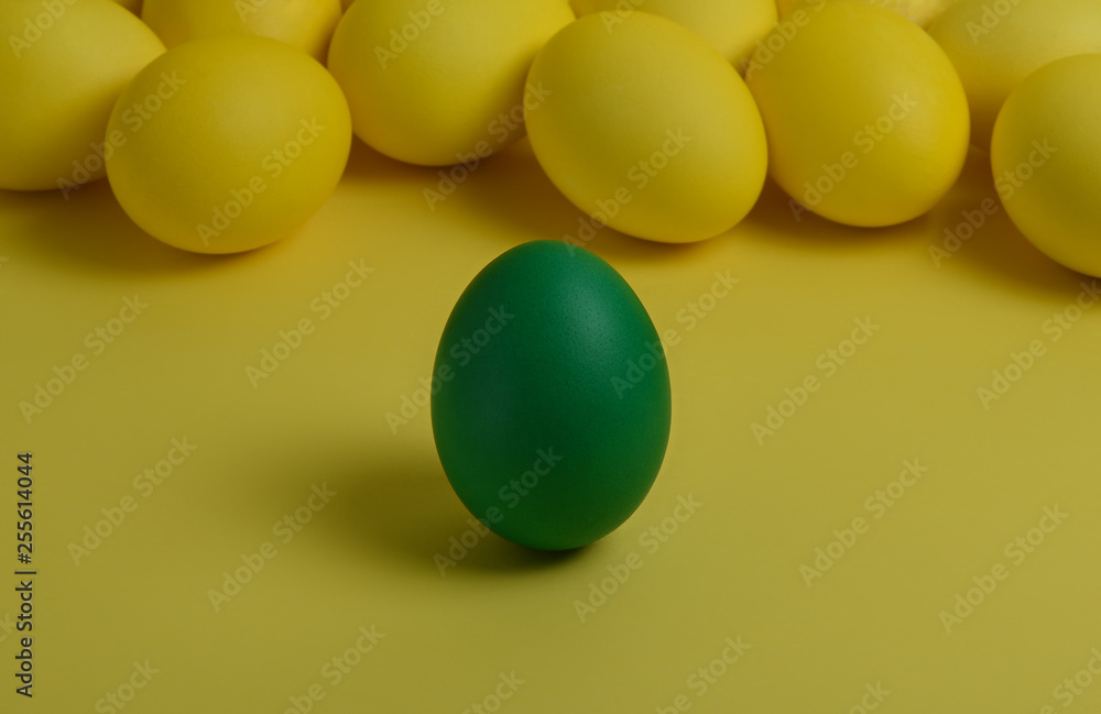One green painted Easter egg stands in front of yellow eggs on a yellow background. Happy Easter holiday card or banner.