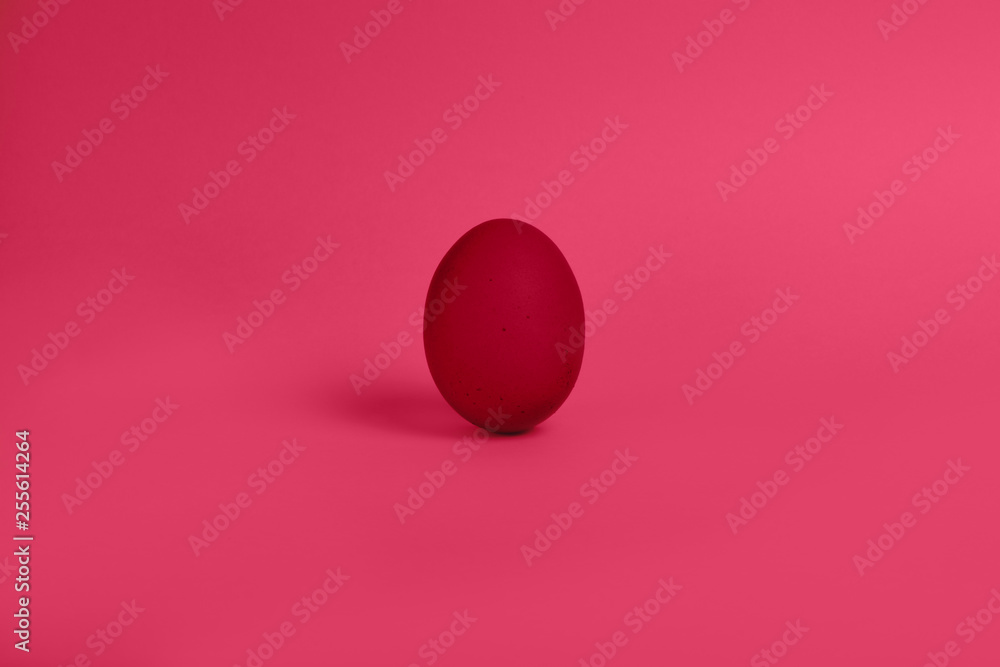 One red painted Easter egg stand on a pink background. Happy Easter holiday card or banner.