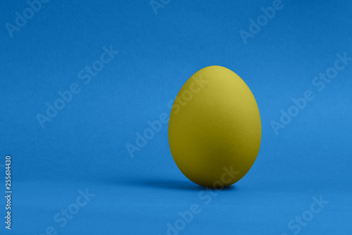 One yellow painted Easter egg on blue background. Happy Easter holiday card or banner. Copy space.
