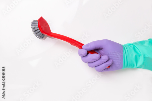 Spring cleaning background. Human hand with a purple and green  household glove is holding a red washing-up brush isolated on a white background. Household chore concept.