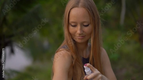 Closeup shot of a beautiful young woman applying an antimosquito repellent spray on her skin. A tropical background. Mosquito defense concept photo