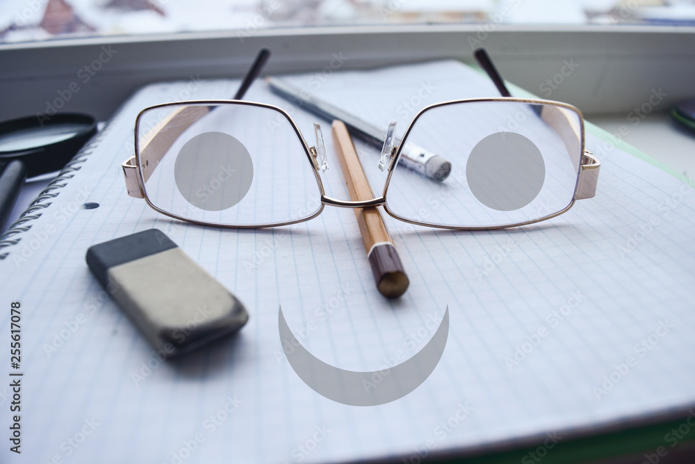 Glasses with eyes and a smile. Drawn graphic elements in the photo with a notebook and pencils. Glasses with eyes and a smile. Drawn graphic elements in the photo with a notebook and pencils.