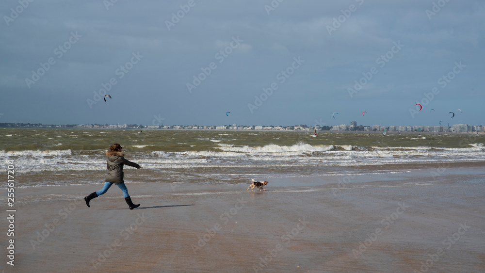 A woman runs after her dog on the beach in winter