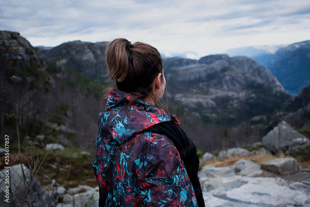 Young adventure girl with a colored jacket contemplating the mountains and the sea in a fjord in norway