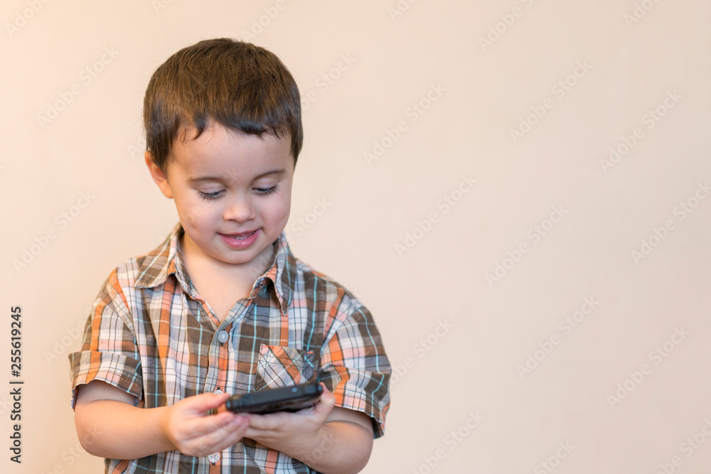 Portrait of a smiling little boy holding mobile phone isolated over light background. cute kid playing games on smartphone. copy space Portrait of a smiling little boy holding mobile phone isolated over light background. cute kid playing games on smartphone. copy space
