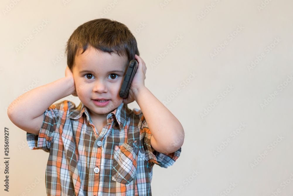 Cute little boy talking by mobile phone on light background. Happy little boy standing and talking on smartphone at home. Technology, education and lifestyle concept. Copy space Cute little boy talking by mobile phone on light background. Happy little boy standing and talking on smartphone at home. Technology, education and lifestyle concept. Copy space